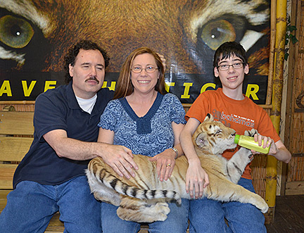 Jordan Diggs (far right) with his parents Parnell and Kim, giving a bottle to a tiger cub spread over their laps.