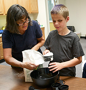 Volunteer Ann assists camper as he measures flour