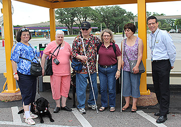 Cheryl, Margo, Milt, Jo, Anahit, and Mark stand at a bus shelter at the Transportation and Ticket Center