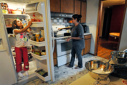 Sienna stands in the refrigerator to find ingredients while Ena cooks.