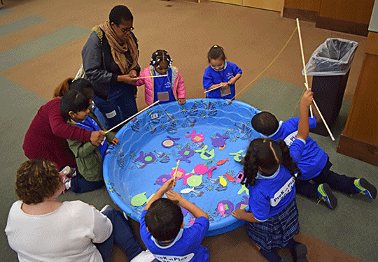 A group of children “fishing” for paper fish in a kiddie pool.