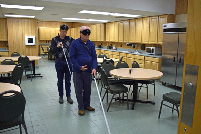 Cane walk in the lunchroom: Corrb O&rsquo;Connor (KY) leads James Bevels (NC) on a Cane Walk under learning shades in the lunchroom of the National Center for the Blind in Baltimore, MD.