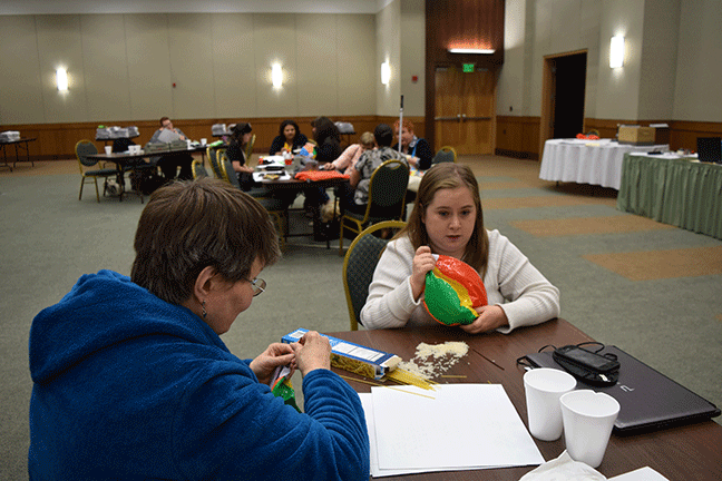 Participants making a beach ball make sound by adding spaghetti noodles and rice: (Left to right) Wendy Bybee (UT) adds spaghetti noodles to a beach ball so that it will make sounds when NFB BELL Academy participants use it in a lesson. Beside her, Katie Chevalier (UT) does the same with rice as the noise-making material.