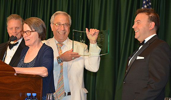 As Mrs. Jernigan speaks, Dan Goldstein smiles and holds up his award, while Marc Maurer and President Riccobono smile and celebrate with him.