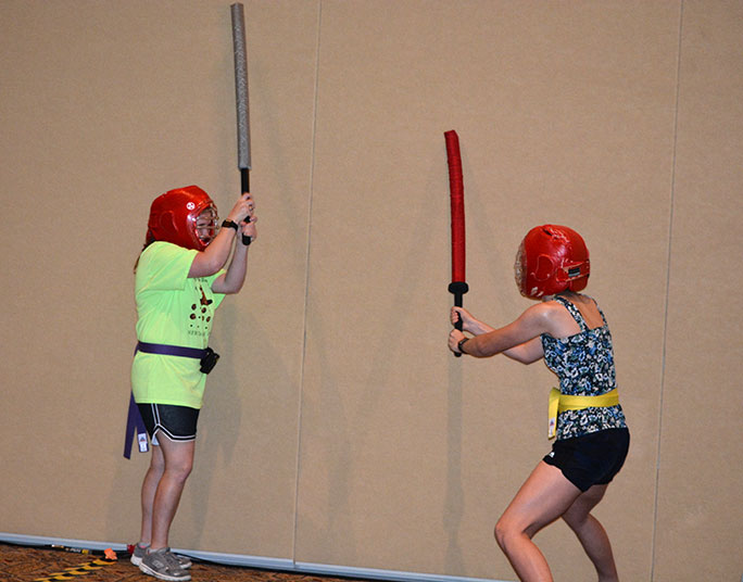 Kayleigh Joiner (TX) and Clare Thomas (TX) face off, head gear on, ready to fence with boffer swards.