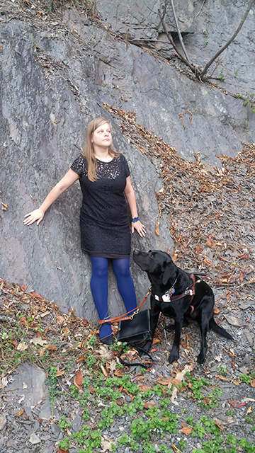 Chancey Fleet enjoys the great outdoors listening as she leans against a rock with her guide dog.