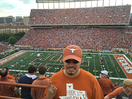 With the football stadium behind him, Jonathan Franks shapes his right hand in the &ldquo;Hook &lsquo;em&rdquo; symbol.