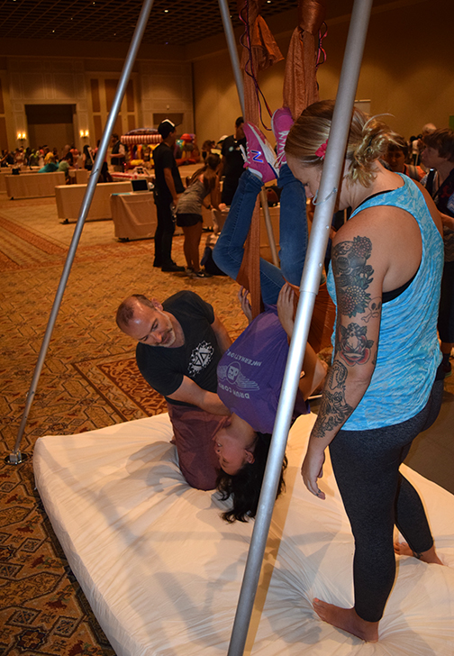 A young Federationist hangs upside down using aerial silks while an instructor coaches her.