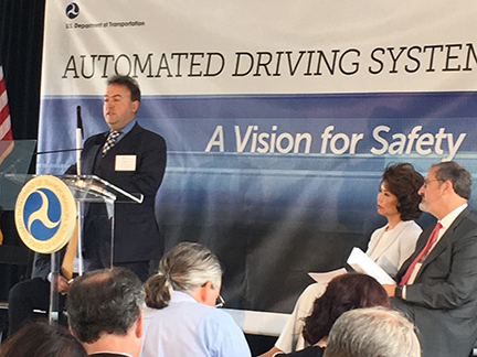 President Riccobono stands at a podium while Secretary Chao and University of Michigan President Mark Schlissel sit off to the side.