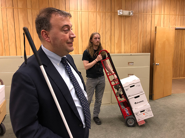 Mark Riccobono smiles as he checks in on the crew moving files and filing cabinets. Staff member, Ryan Pugh, stands in the background with a cart full of file boxes.