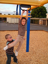 A little boy gives Milagro a push to start her sliding on the metal beam of a jungle gym.