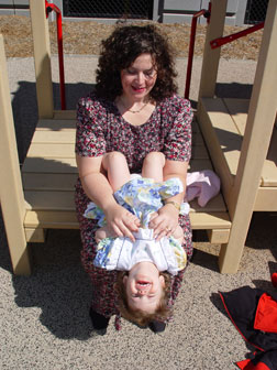 During a visit to the playground, Kendra sits on her mother's lap and playfully leans back as far as she can.