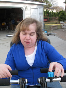 Rachel is seated on a tandem tricycle with her hand on the bell.