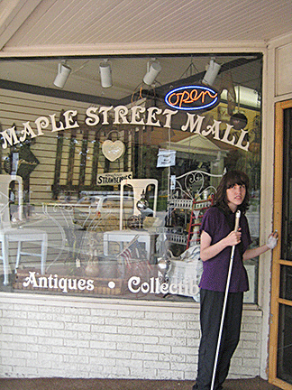 A teenage girl with a cane stands outside a shop loaded with antiques and collectibles.