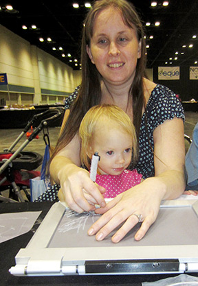 Holding her daughter in her lap, a mother draws a raised-line picture.