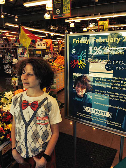 Josh Goldenberg stands in a supermarket with a poster about The Joshua Project in the background.