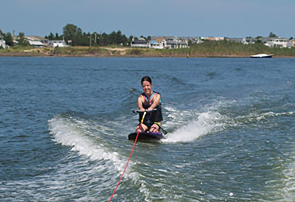 Holding the tow rope, Serena kneels on the knee board, grinning broadly.