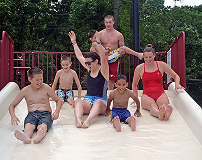 Laughing group of kids and counselors prepare to go down a slide.