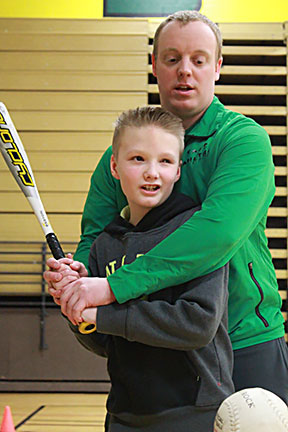 A counselor teaches a boy to swing a baseball bat.
