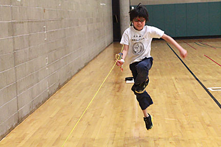 A boy skips, following a rope to which his wrist is tethered.