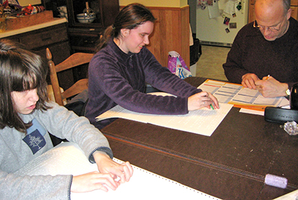 Jenny and Anna Schuck read Braille at the kitchen table while Nathan Schuck fills out a form.
