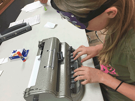 Liz uses a Braillewriter under sleepshades at Nebraska BELL.
