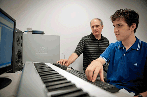 Bill McCann sits at a keyboard with a student.