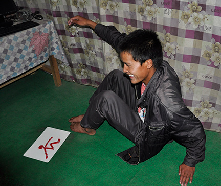 A young Nepalese man imitates the body position of a tactile stick figure.