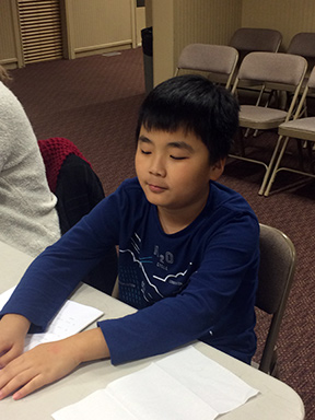 Isaiah Rao reads Braille pages at a table.