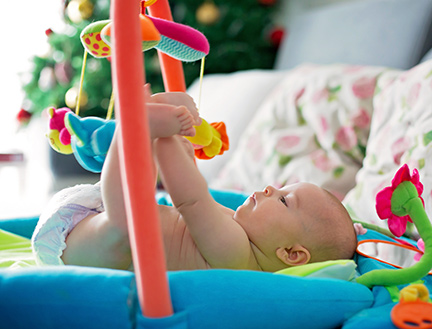 A baby lies on his back, playing with toys suspended above him.