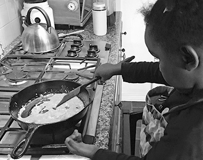 Lizzy stirs eggs in a skillet on the stove.