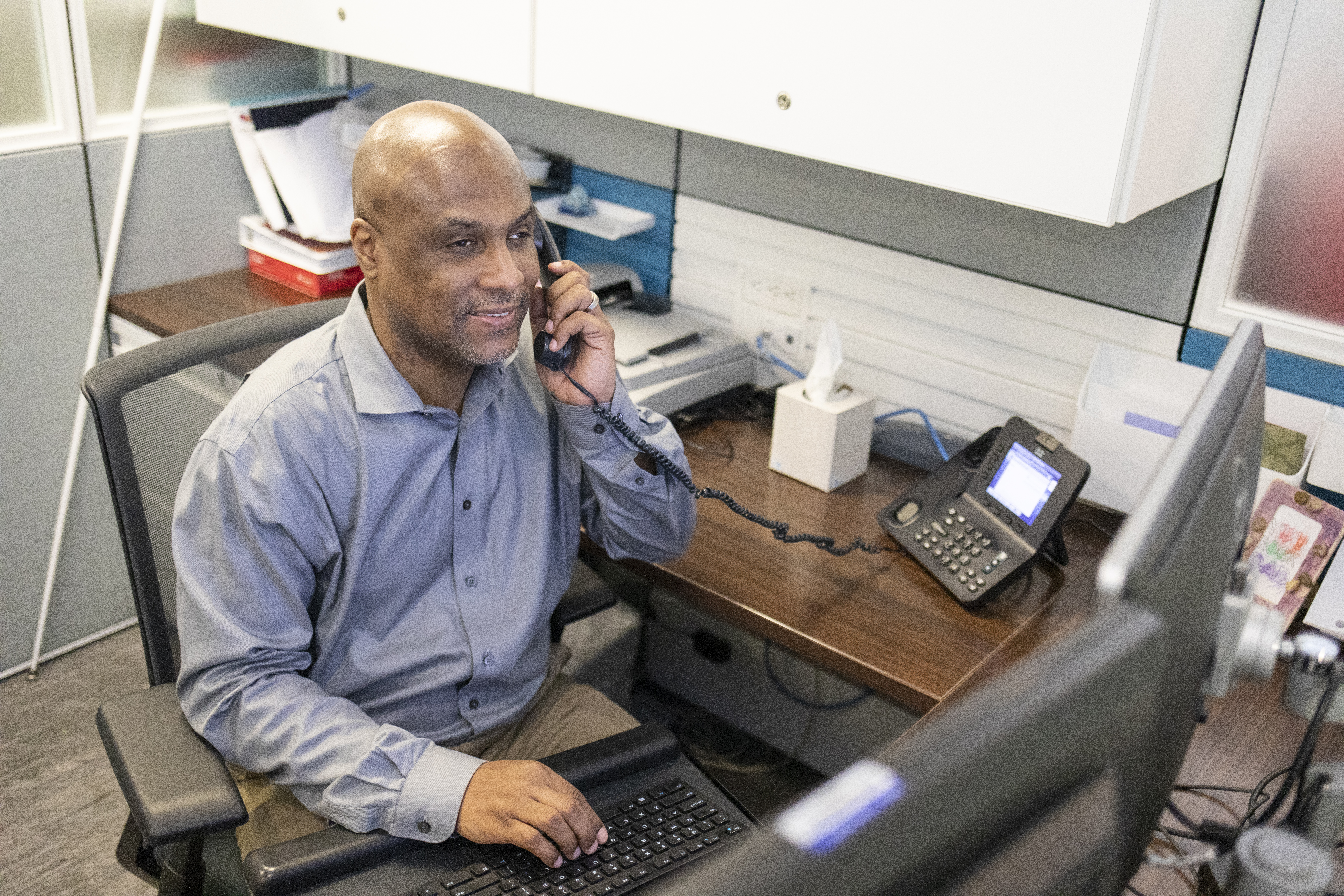 A blind man answers the phone in his office cubicle