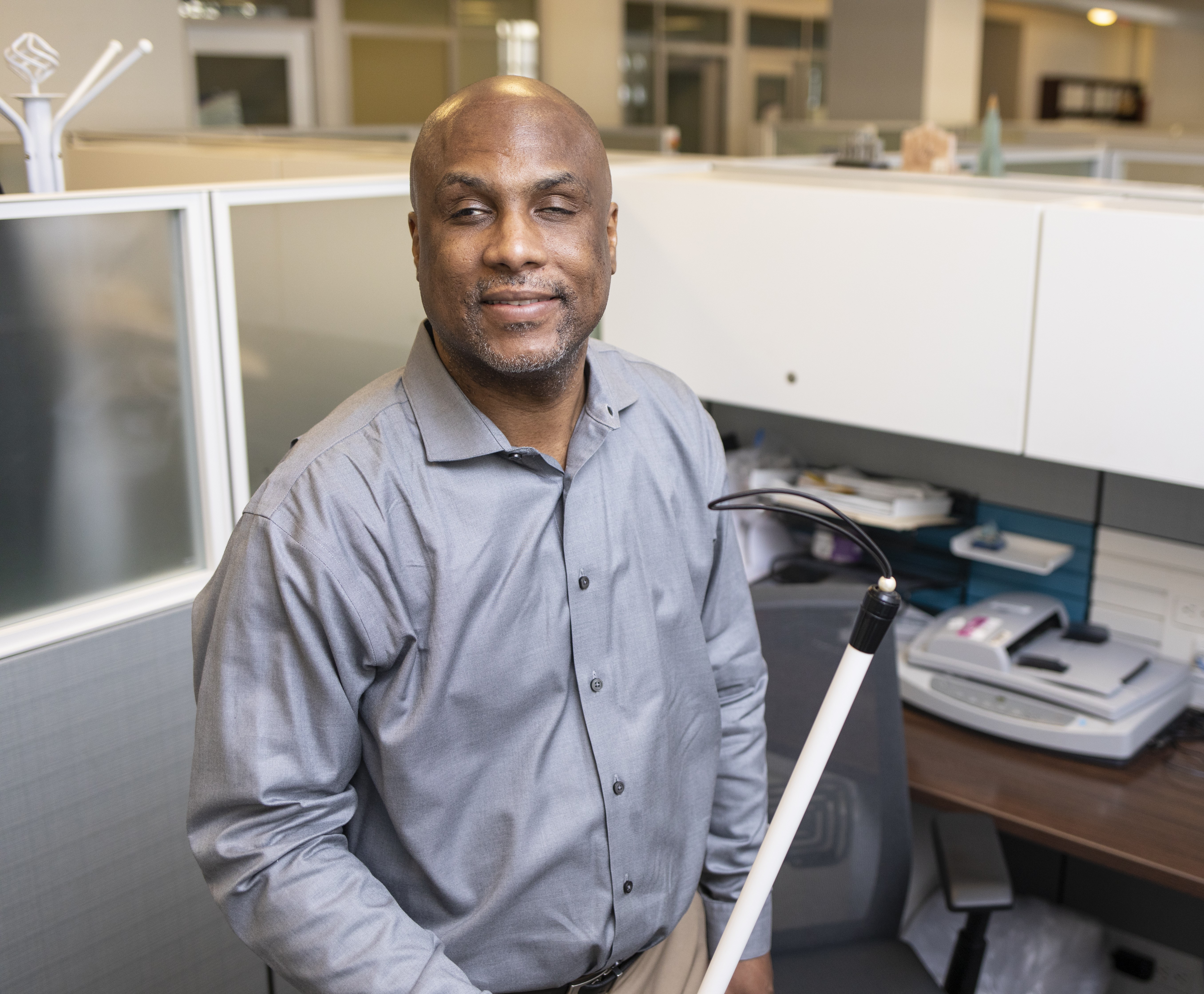 A blind man stands in front of a office cubicle