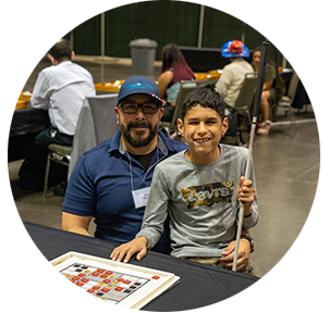 A blind boy sits on his father's lap in the NFB National Convention exhibit hall