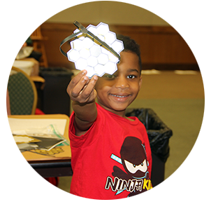 A STEM2U participant smiles and holds up a tactile model of the mirror of the James Webb Space Telescope