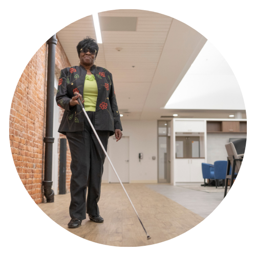 Black woman walks with white cane around Jernigan Institute family room