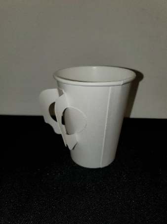 A white paper cup, with its two attached rings folded out away from the cup itself to form a handle. The cup is sitting upright on a base, with the handles on the left side.