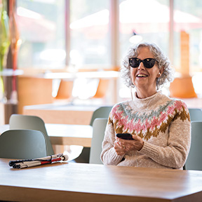 A senior woman smiles as she listens to NFB-NEWSLINE in a cafe.