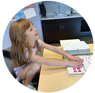 A young NFB BELL student smiles as she checks out a tactile book.