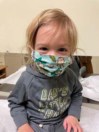 Kadyn, wearing a mask with monkeys on it, sitting at the doctors office for his two year appointment.