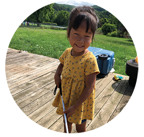 A blind toddler smiles while holding her long white cane.