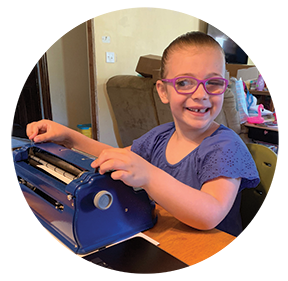 A young blind girl smiles as she works on a Perkins Brailler.