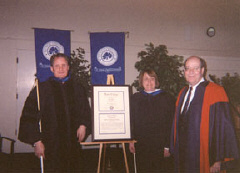 Three people are pictured in academic regalia.  Joanne Wilson holds her honorary degree
