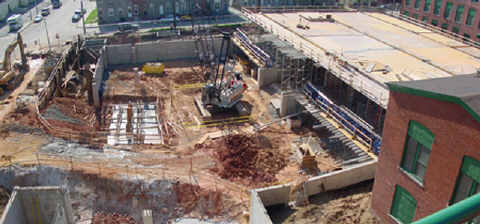 Panoramic view of the National Center for the Blind construction site taken on May 1, 2002.   About 50 percent of the two parking levels are visible, and the third level is well started.  The large track crane at the center of the picture will soon be withdrawn through the remaining gap in the foundation perimeter wall that can be seen at the left edge of the picture.   The pools of rain water with planks stretched across them are actually the three elevator shafts, which have been sunk even deeper than the foundation.