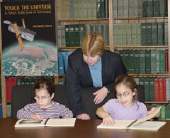Mikaela Stevens (left) and Makenzie Stevens (right) examine the Braille book, TOUCH THE UNIVERSE, while author Noreen Grice leans above them.