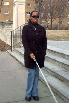 Michele Gittens uses her cane under sleepshades outside BLIND, Inc.
