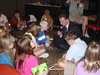 President Maurer sits cross-legged on the floor with blind children gathered around him.