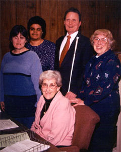 NFB President Marc Maurer stops by for a chat with busy Braille Readers Are Leaders volunteers. On the left are NFB members Bernice Lowder and Mary Kuforiji, and on the right are Rolling Hills Federated Women's Club members Katherine Carbonneau and Aline Norris.
