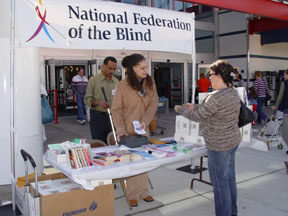 Members of the NFB of Maryland student division, Muttasin Fadl (handing out Braille alphabet cards to shoppers), Lydia Richardson, and Presient Mika Bowers at a Wal-Mart information table.