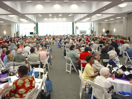 On May 20,2004, the third annual NFB-sponsored senior fair took place at the National Center for the Blind.   This year for the first time the setting was Members Hall on the fourth floor of the new Jernigan Institute.   Pictured here, the crowd is seated at tables to consume 420 box lunches and enjoy a lively program.
